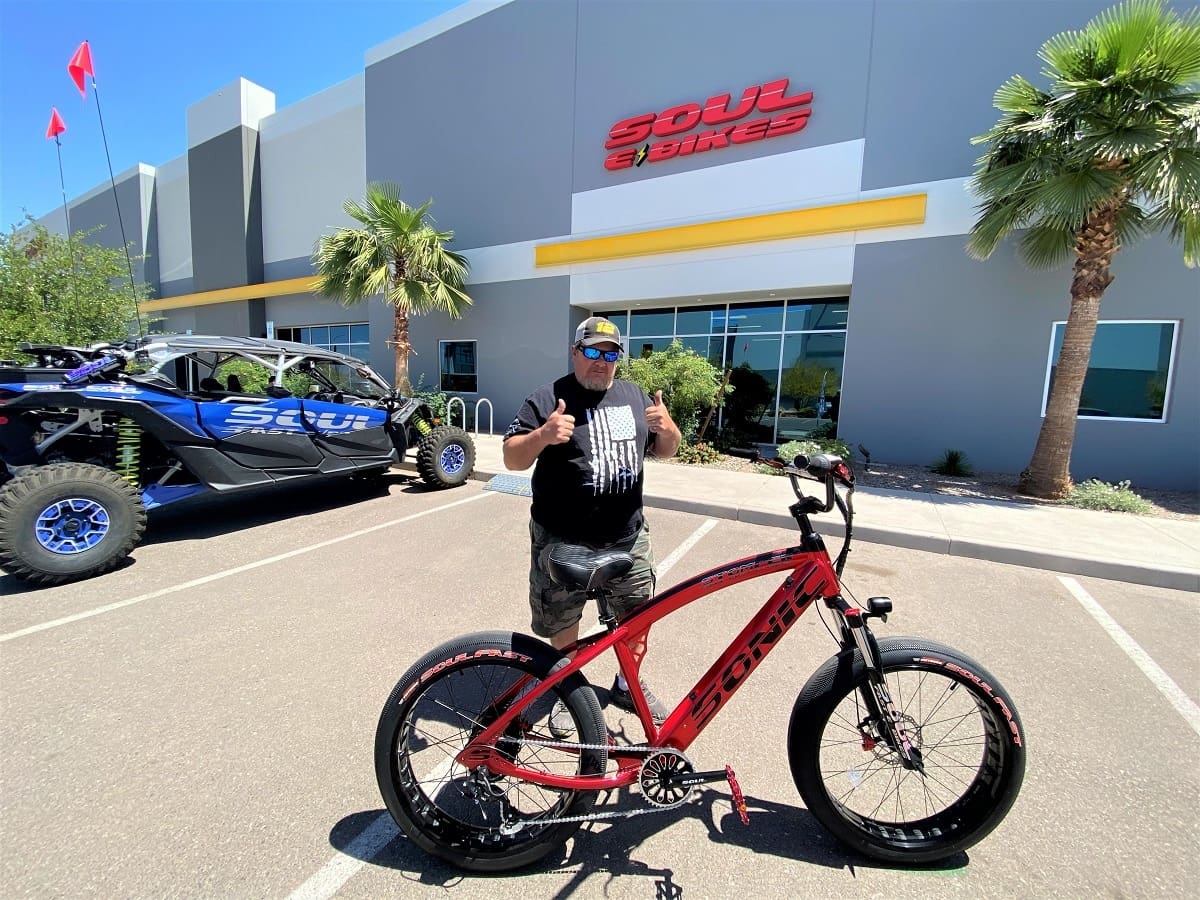 Man posing with red bicycle outside store.