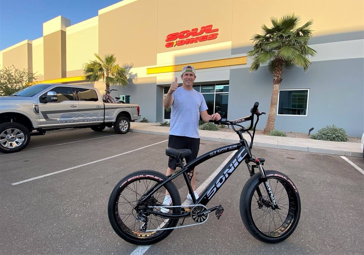 Person thumbs up beside black electric bicycle.