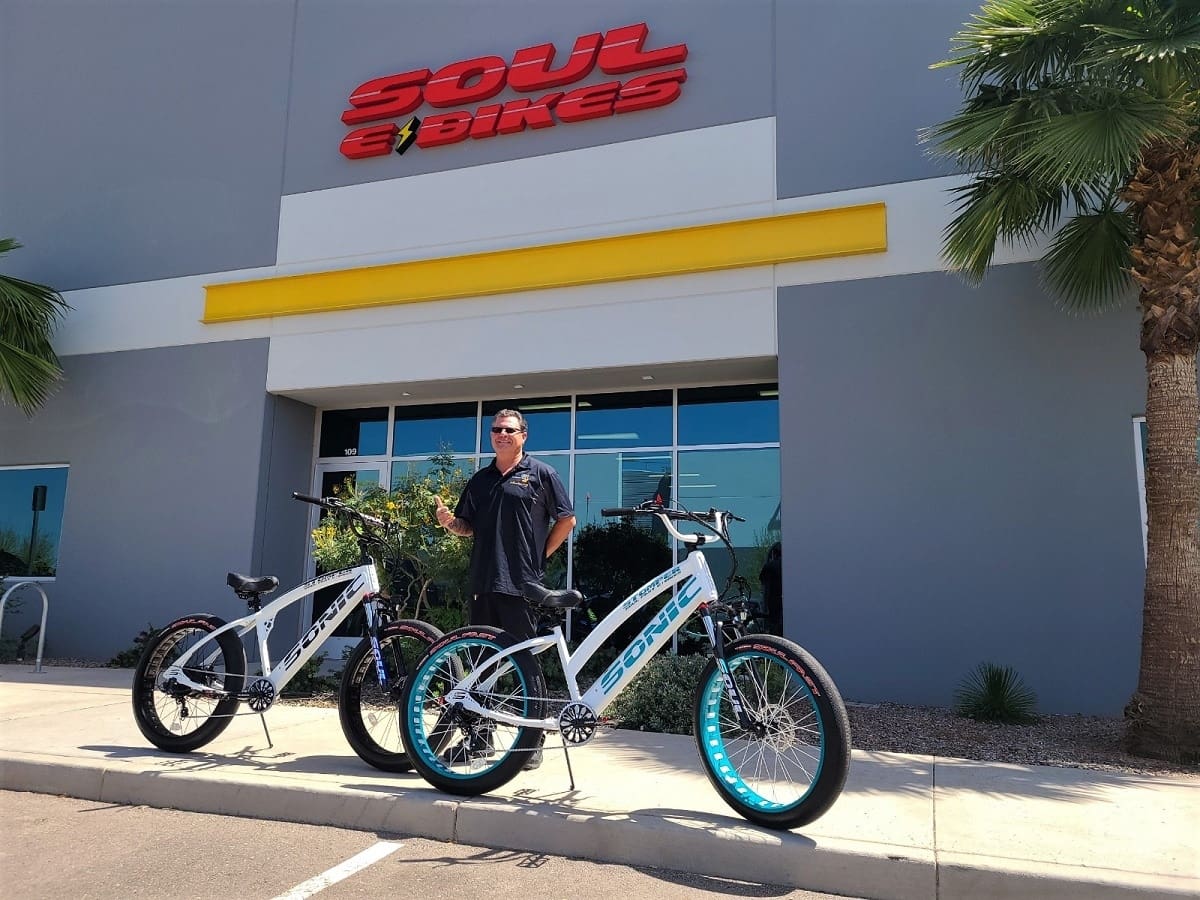 Man standing with two bicycles outside store.