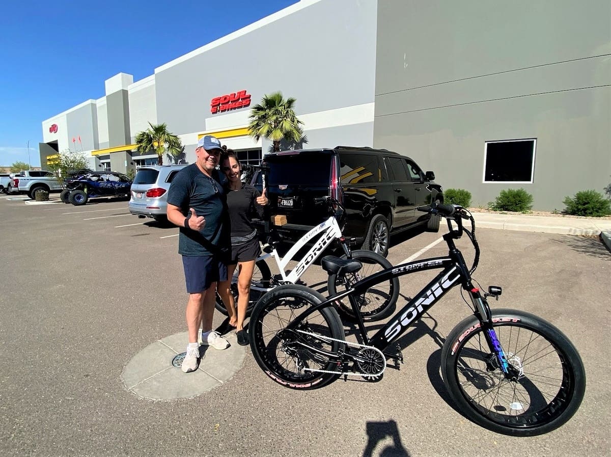 People posing with electric bikes outside store.