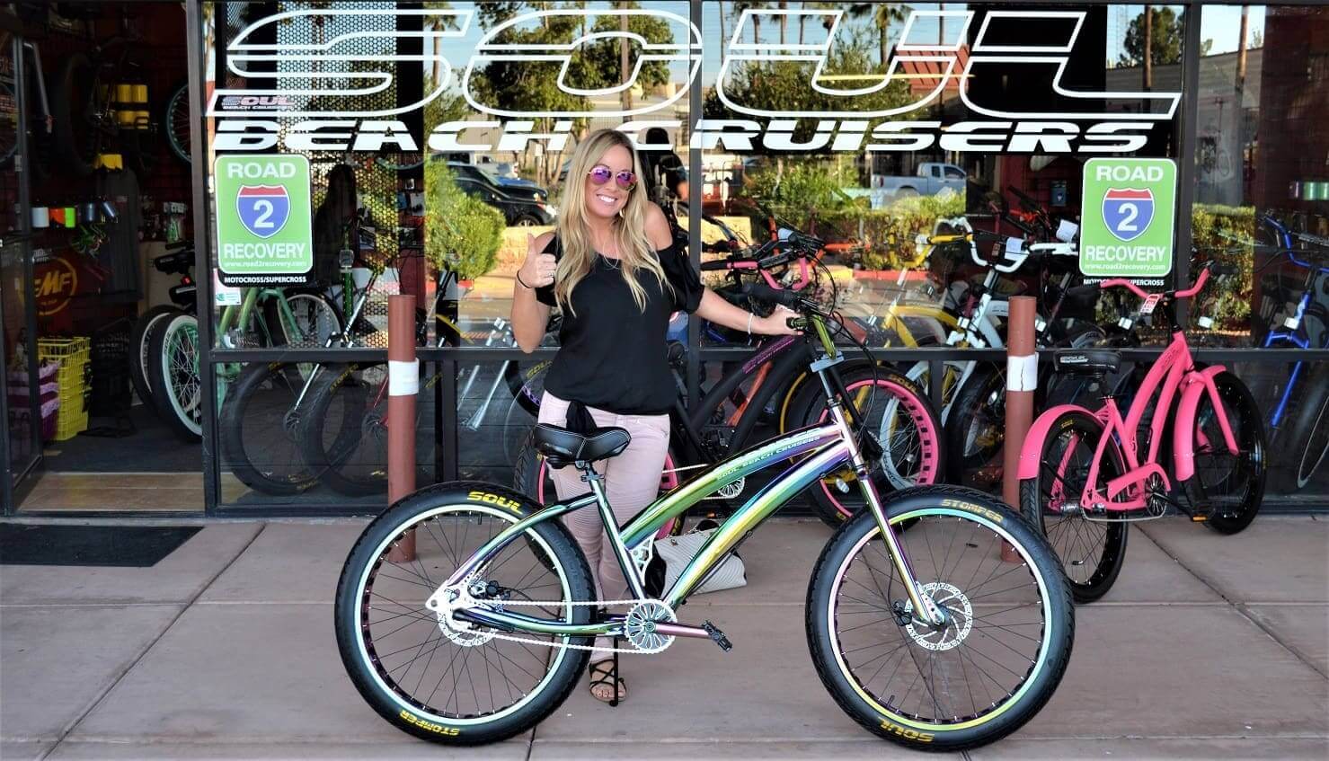 Woman posing with colorful bicycle outside shop.