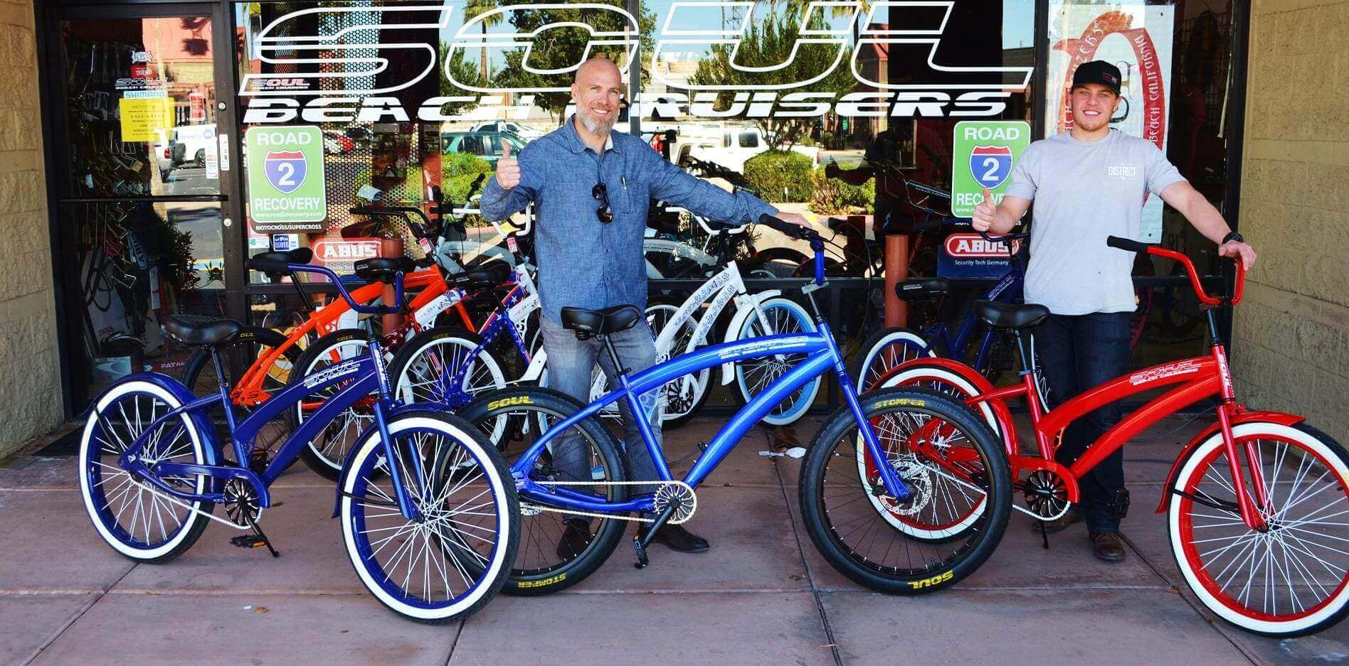 Two people showcasing colorful beach cruiser bikes.