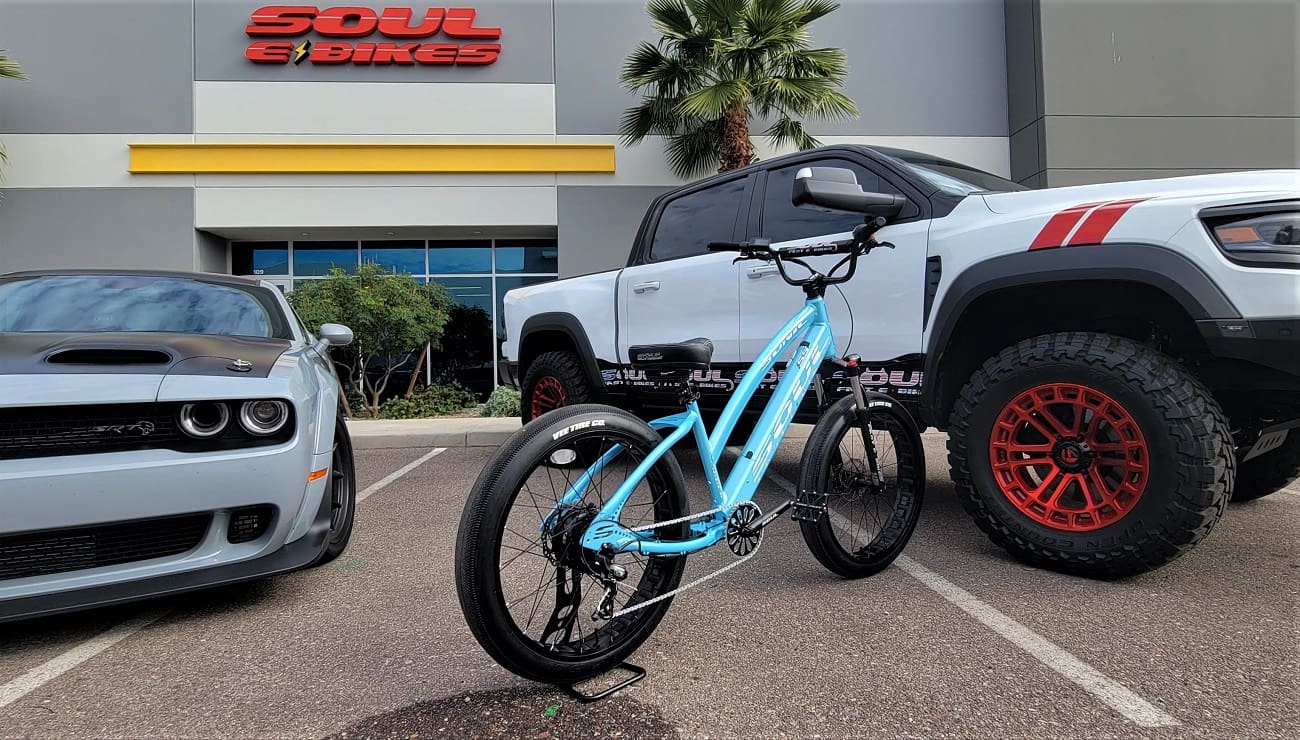 Blue e-bike between car and truck.