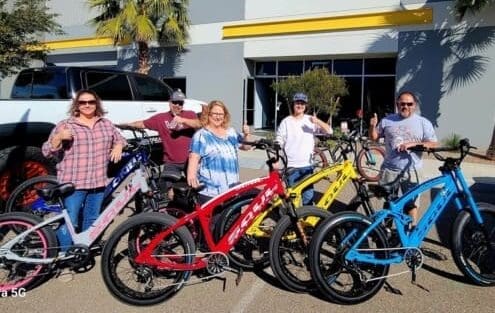 Group posing with colorful electric bicycles outside.