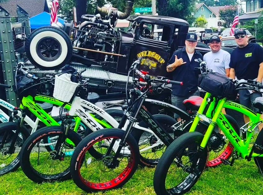 Three men alongside hot rod and e-bikes