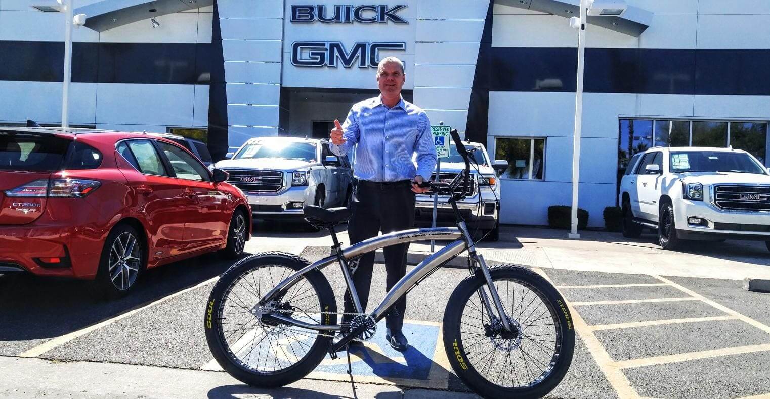 Man with bicycle outside Buick GMC dealership.