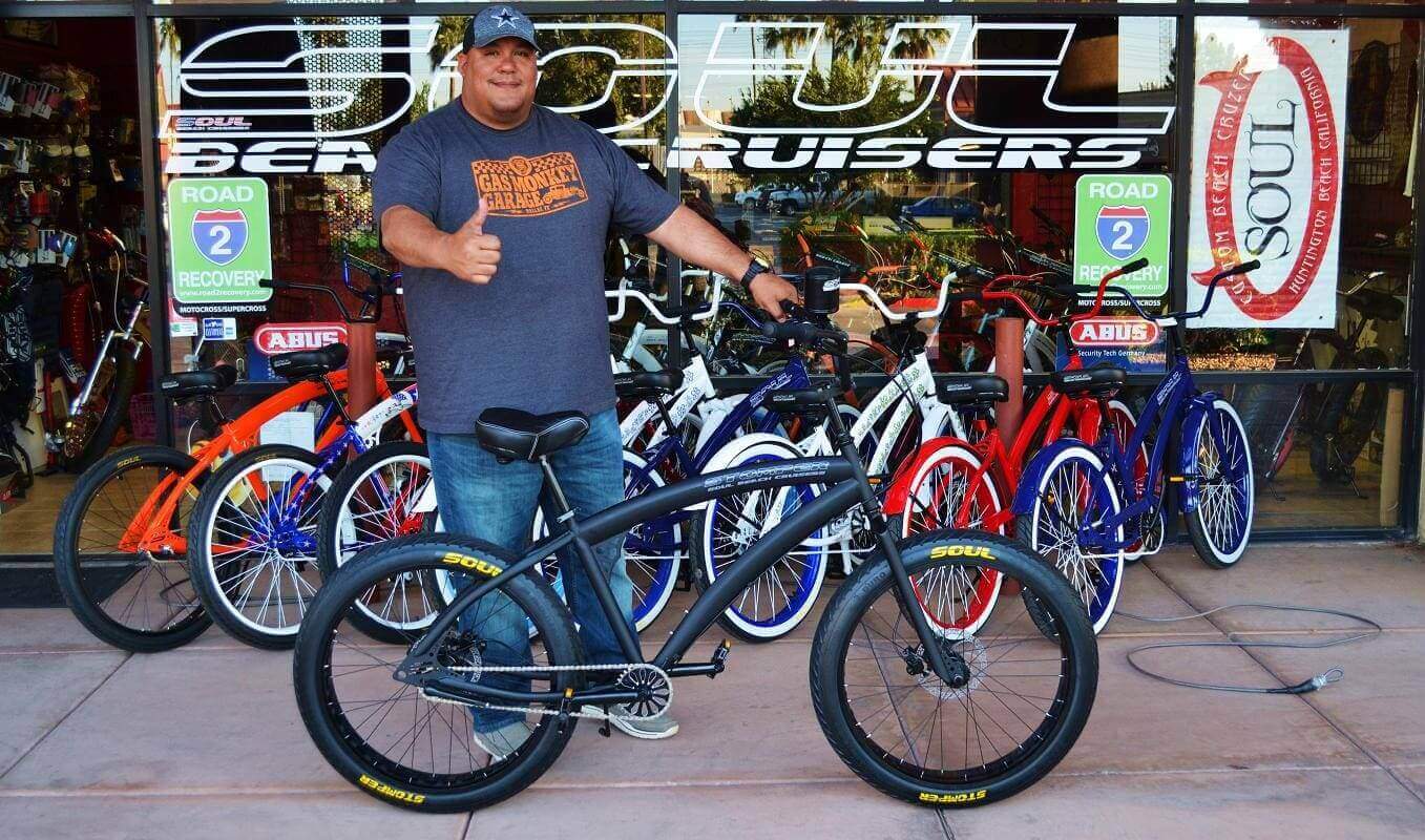 Man posing with a bicycle outside store.