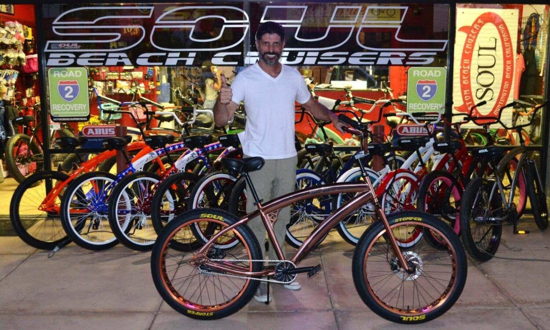 Man posing with bicycle outside bike shop.