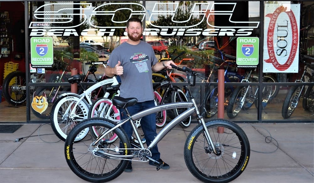 Man smiling with a bicycle outside shop.