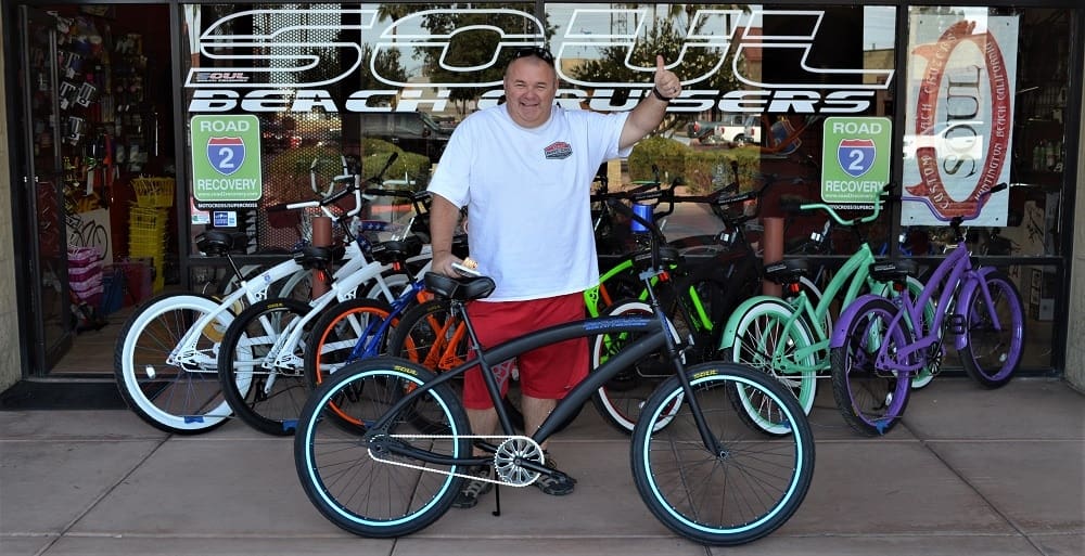 Man posing with bicycles outside a shop.