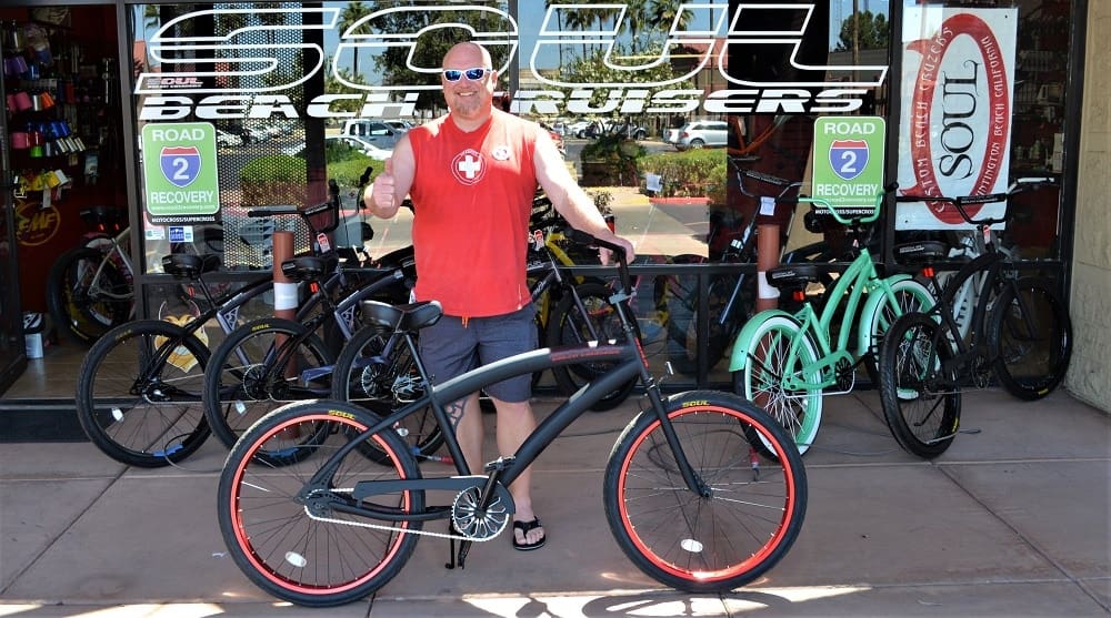 Man posing with bicycle outside bike shop.