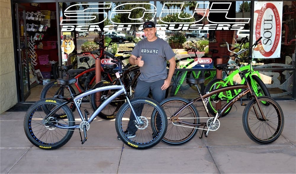Man posing with colorful beach cruiser bicycles.