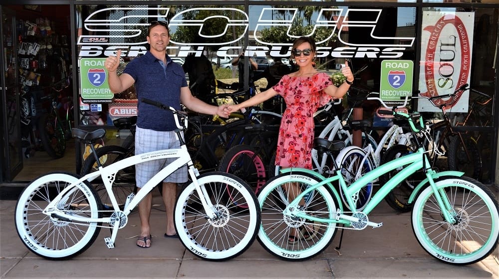 Two people holding bikes outside bike shop.