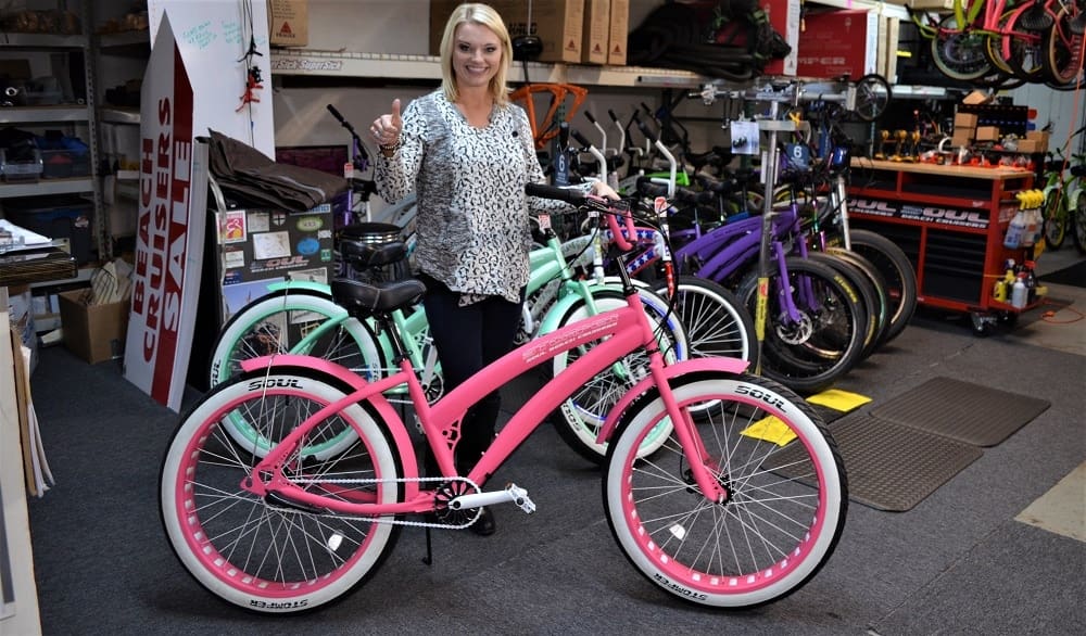 Woman standing with colorful beach cruiser bicycles.