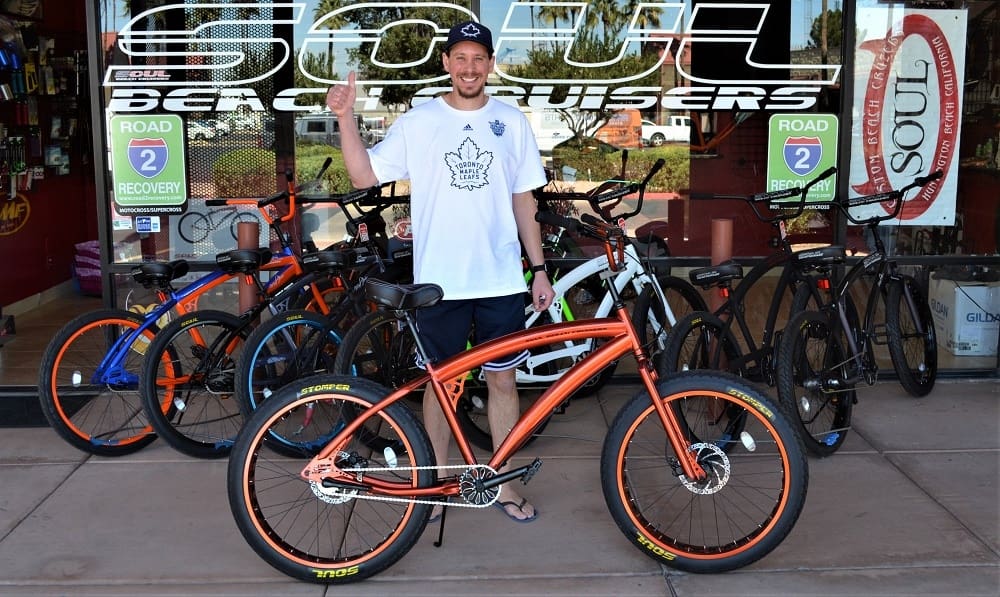 Man standing with orange bicycle, store background.