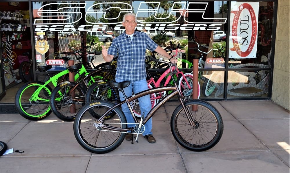 Man standing with black bicycle outside store.