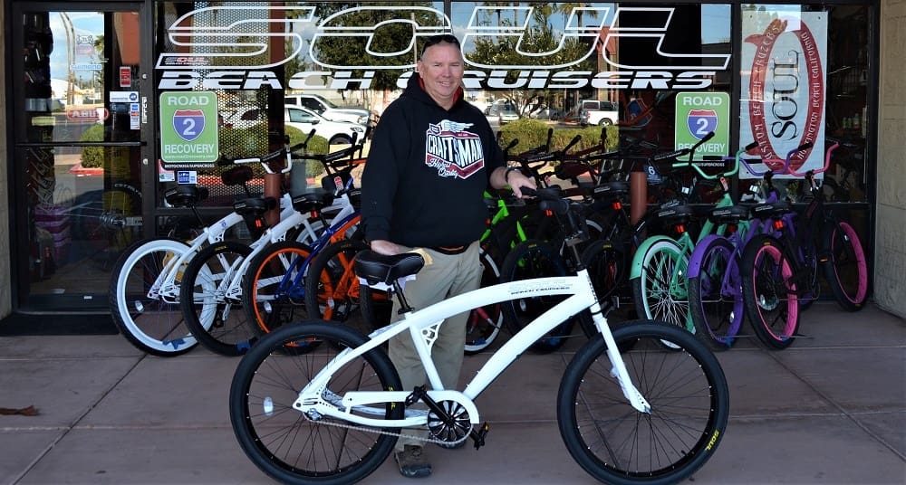 Man standing with a white bicycle outside store.