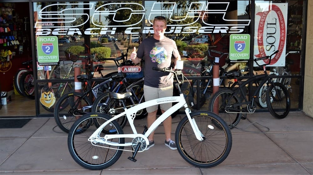 Person holding white bicycle outside shop.