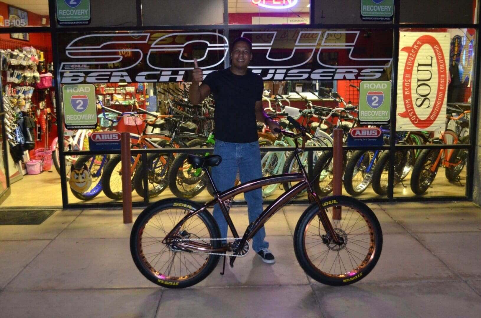 Man posing with bicycle outside a shop.