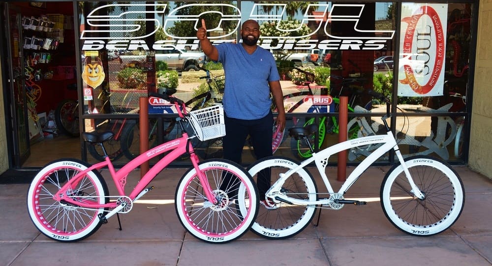 Man posing with two colorful cruiser bicycles.
