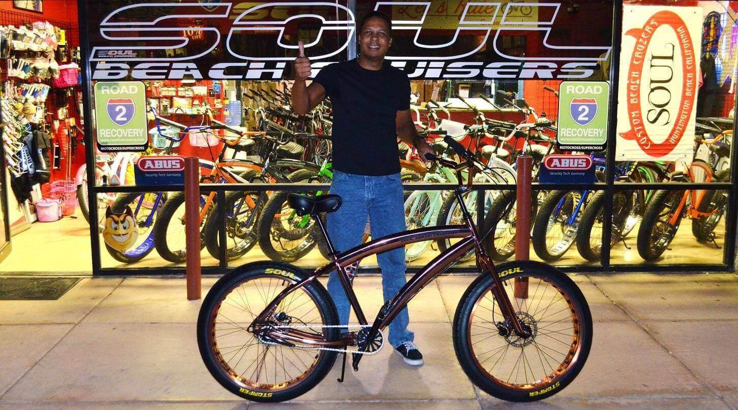 Man posing with bicycle outside bike shop.