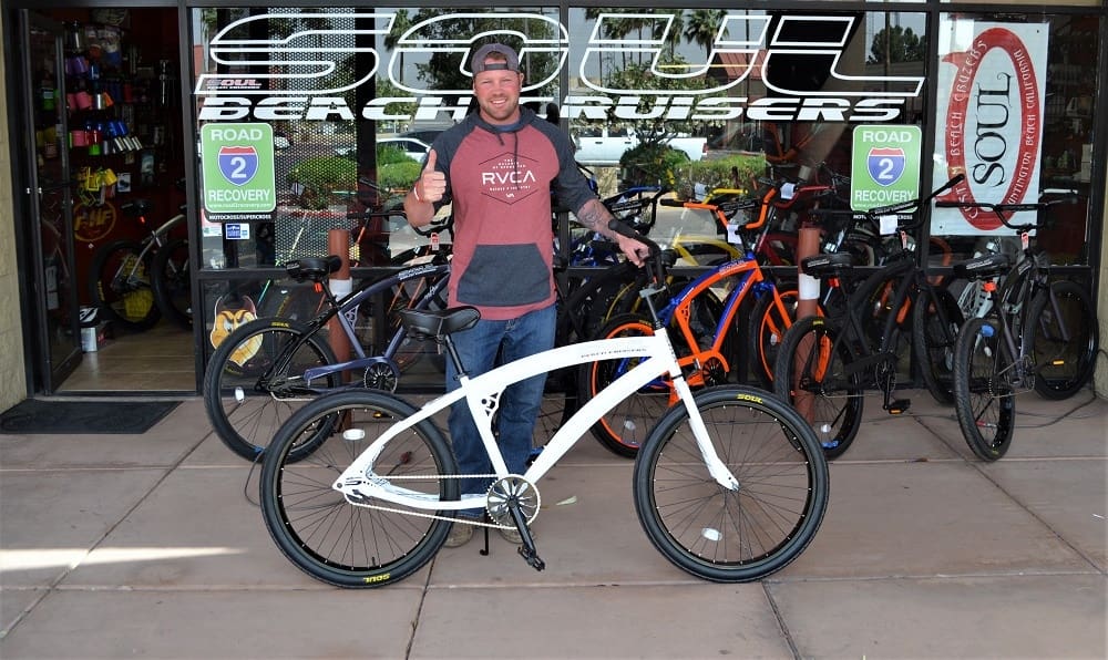 Man standing with a bicycle outside shop.