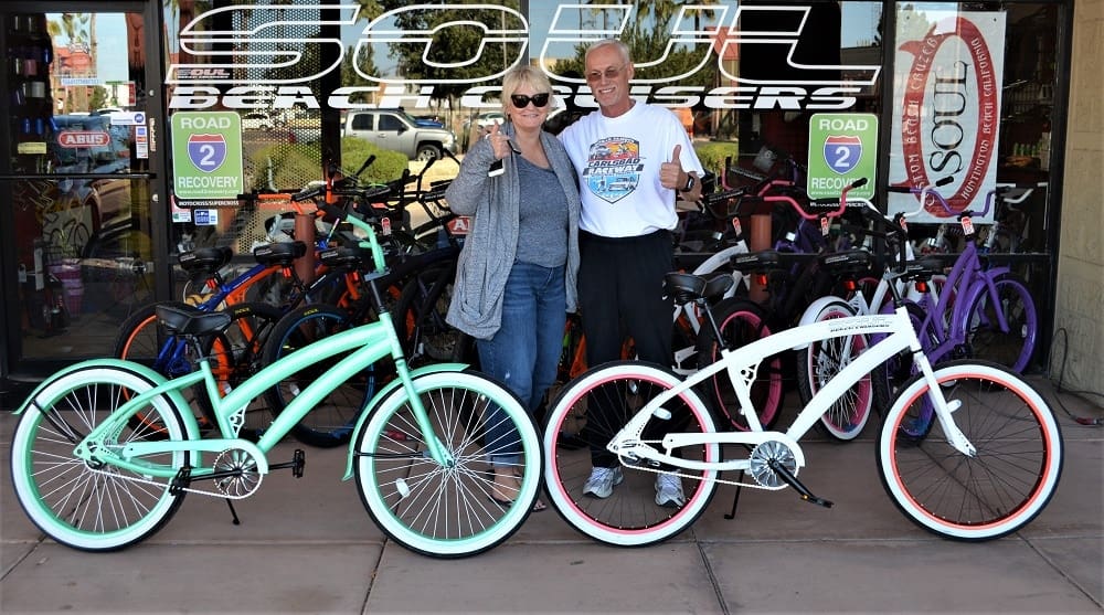 Two people posing with colorful bicycles.