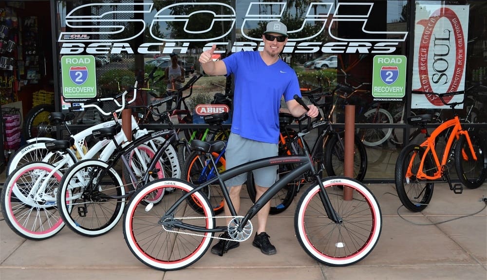Man standing with cruiser bicycles at store.