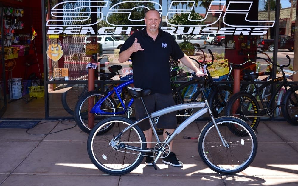 Man posing with a bicycle outside shop.