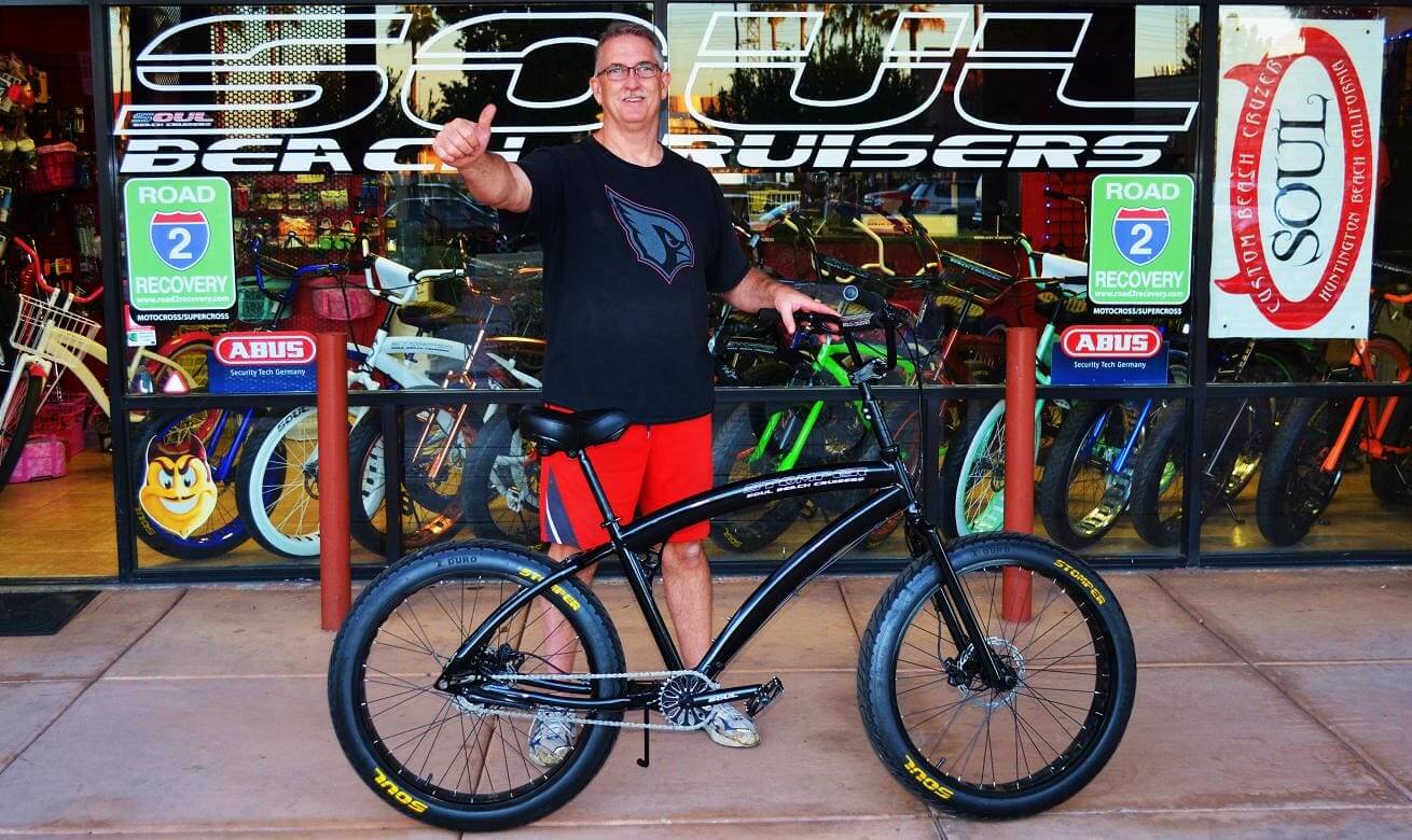 Man posing with bicycle outside bike shop.