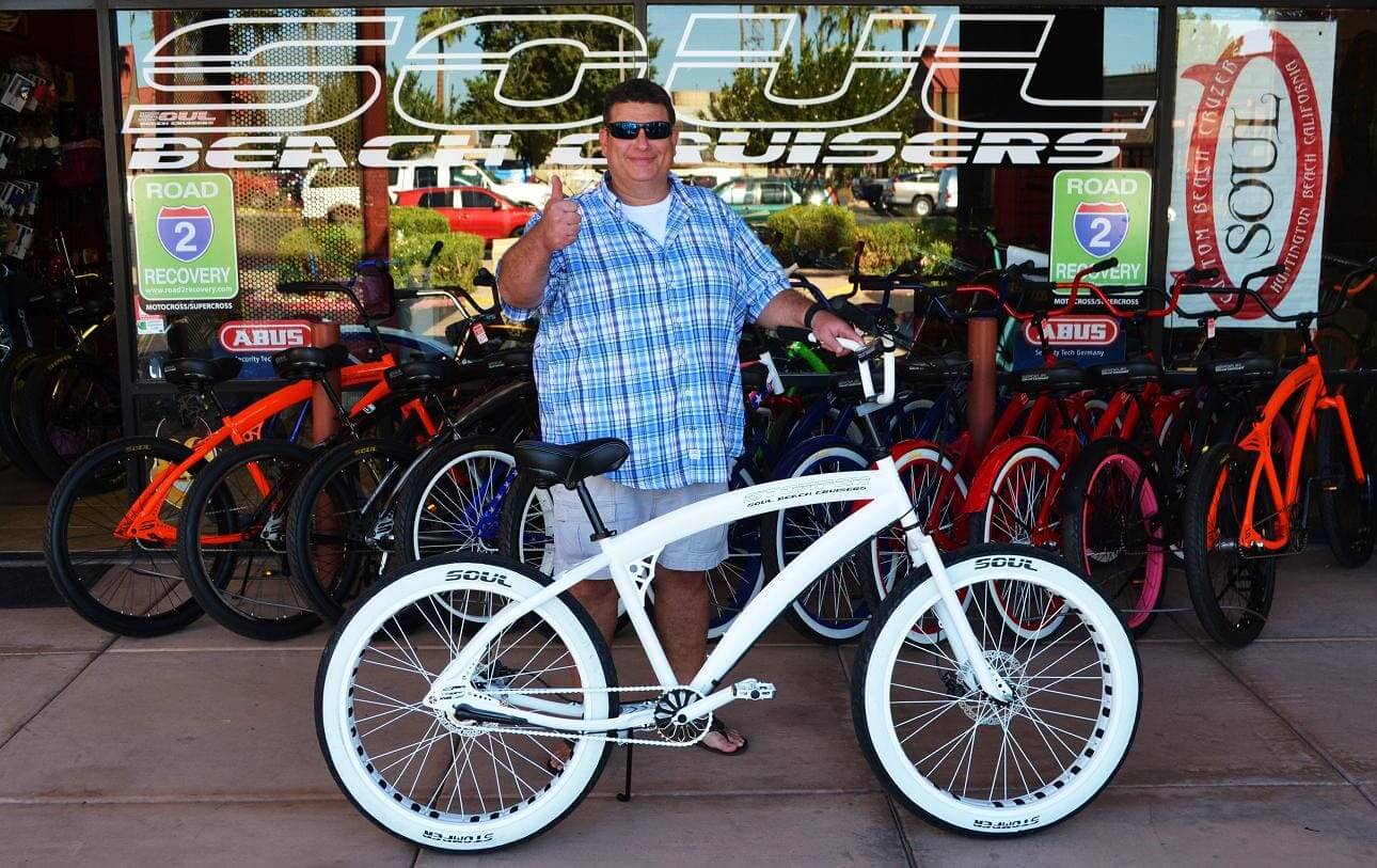 Man with white bicycle in front of shop.