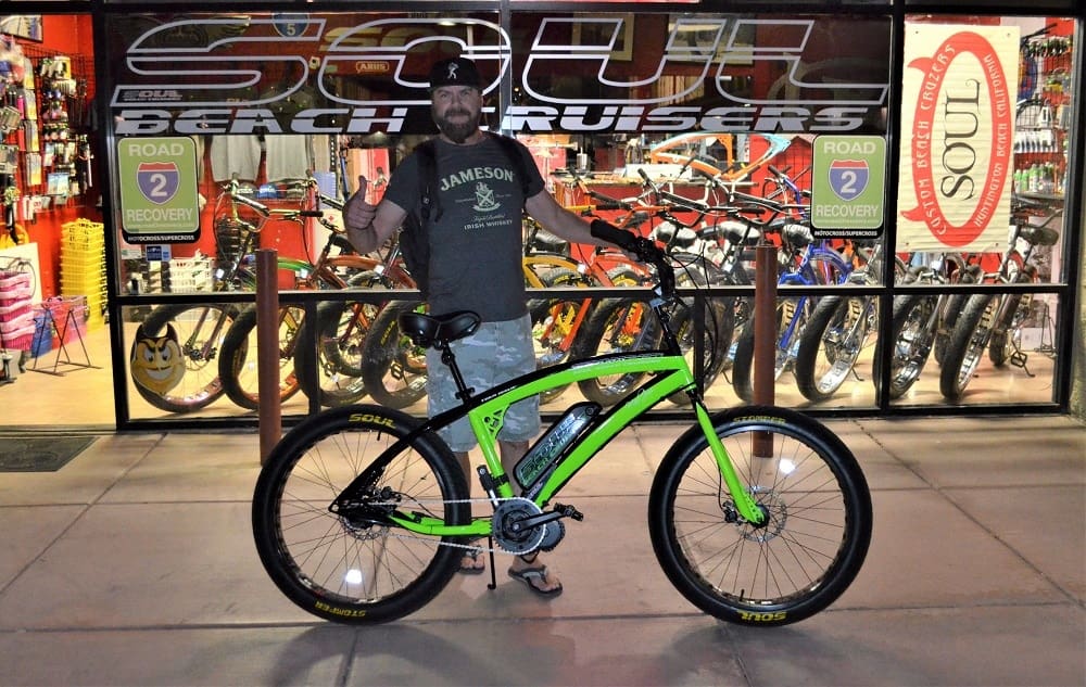 Man with green bicycle outside bike shop.