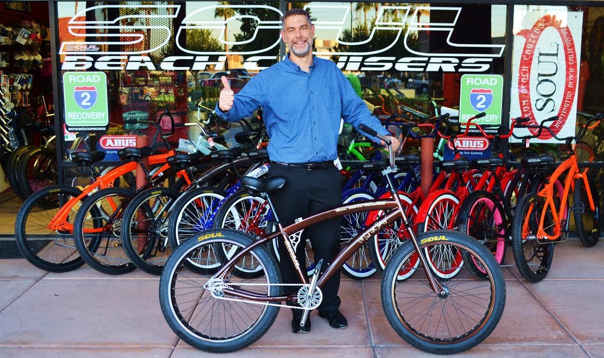 Man standing with bicycle outside bike shop.
