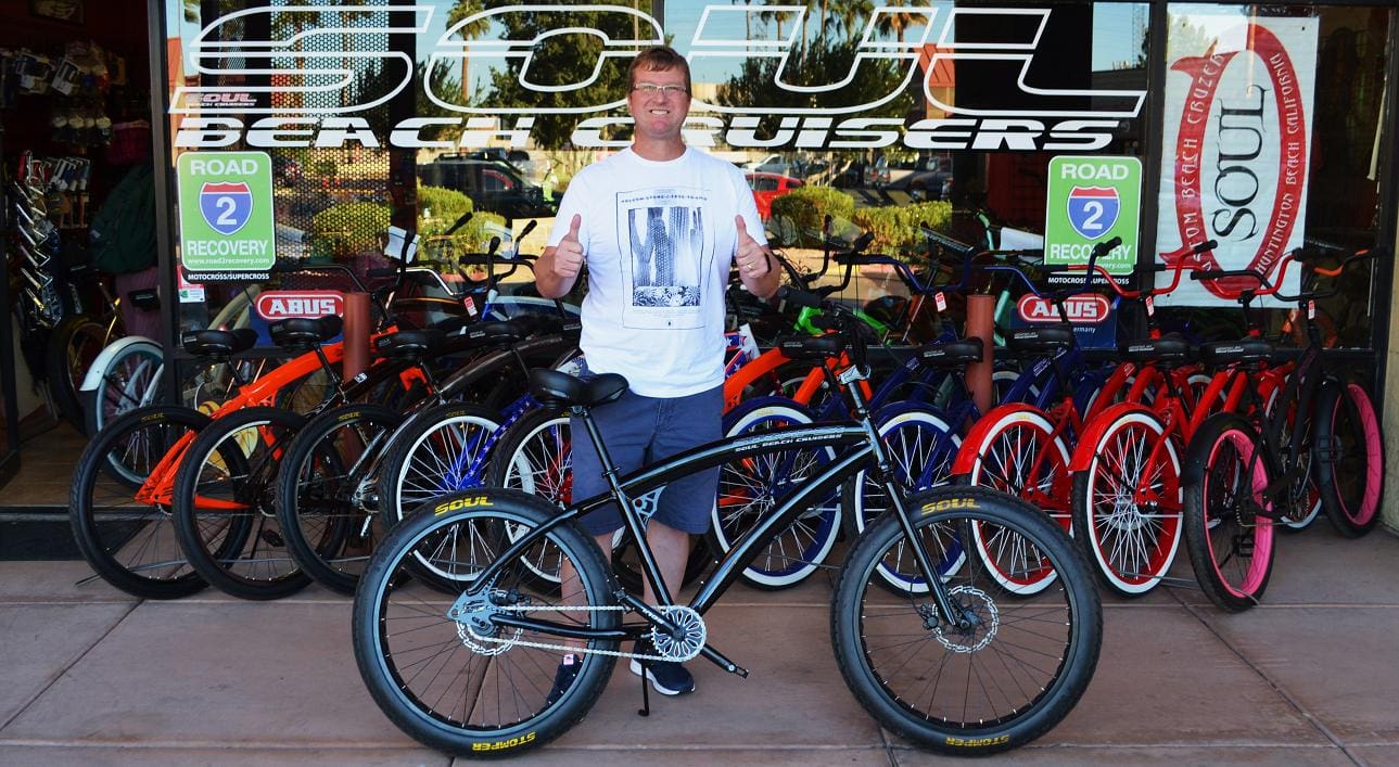 Man posing with bicycle outside a shop.