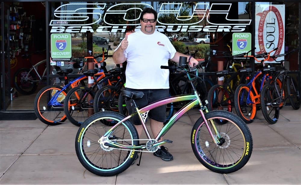 Man posing with colorful beach cruiser bicycle.