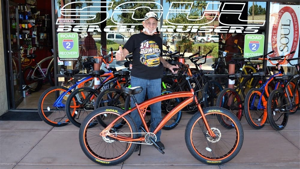 Man standing with orange bicycle outside store.