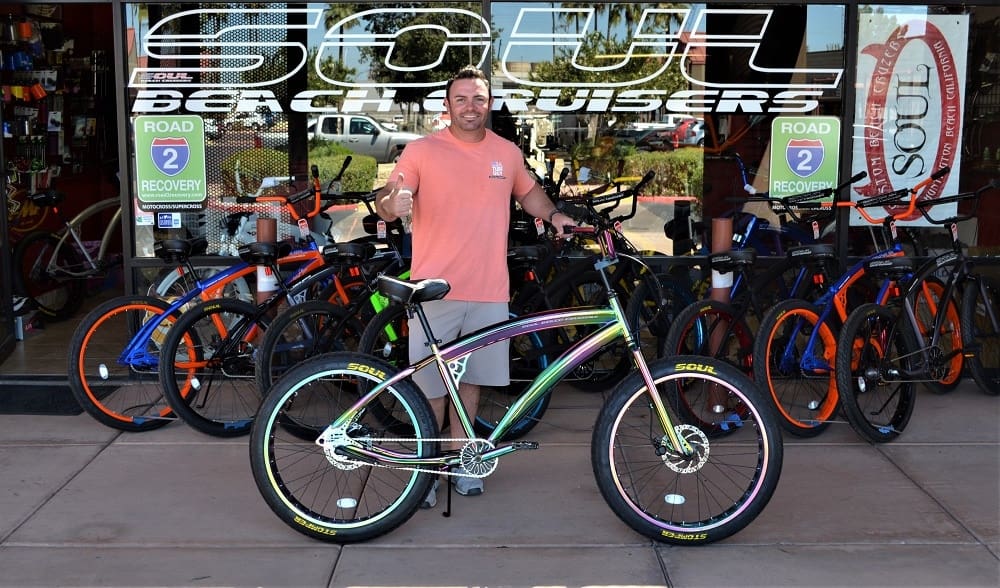 Man standing with colorful bicycle outside shop.