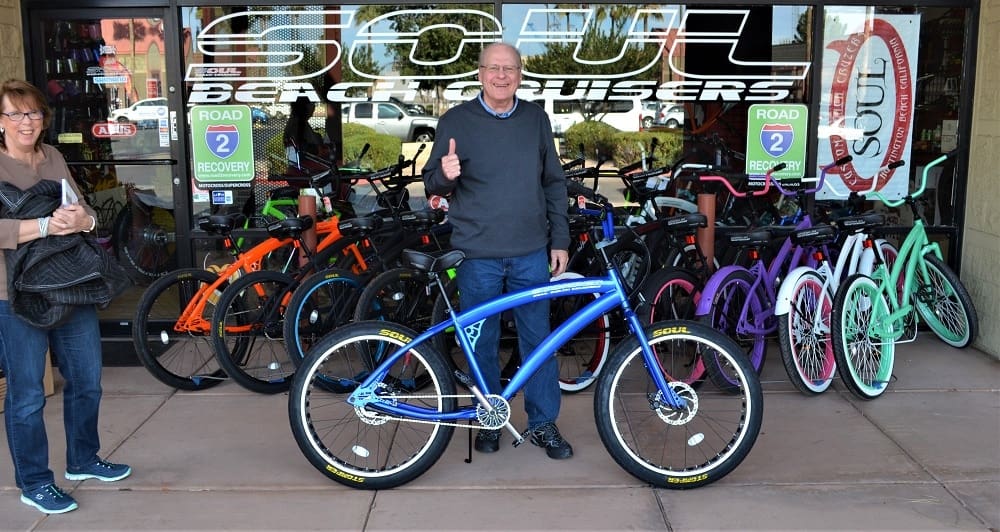 Man with blue bike outside bicycle shop.