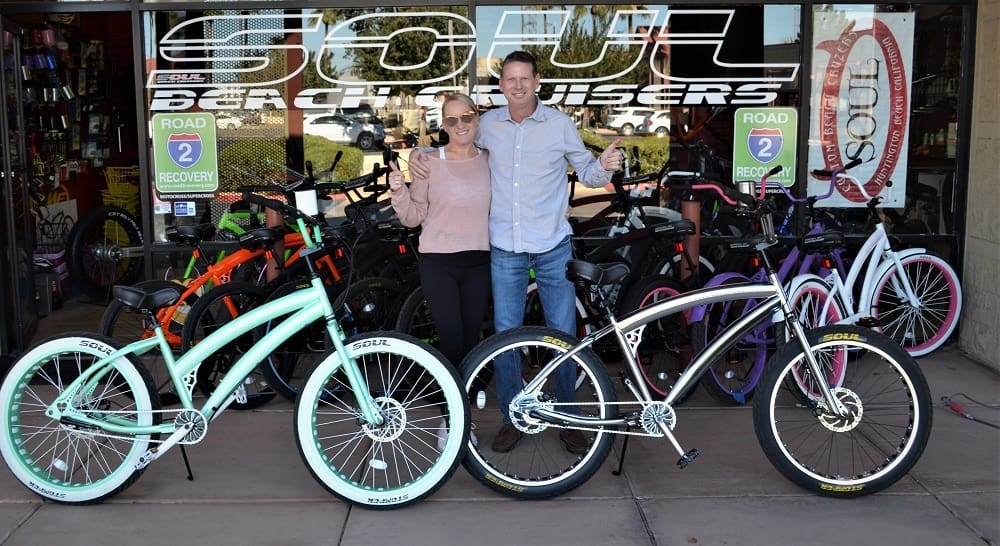 Two people standing with beach cruiser bikes.