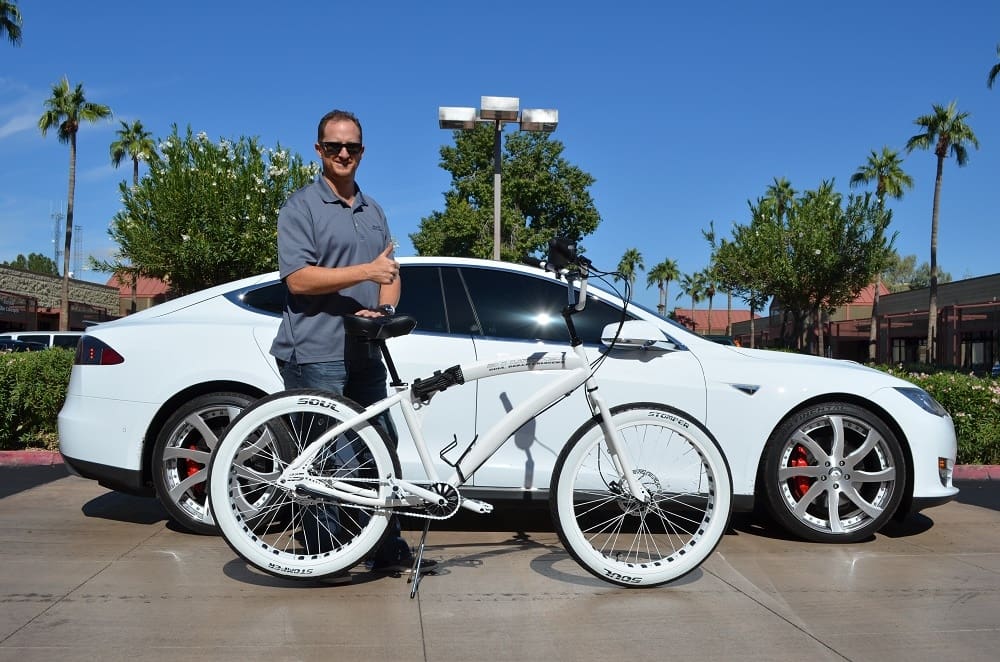 Man with white bicycle and car outside.