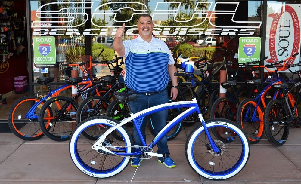 Man posing with blue and white bicycle.