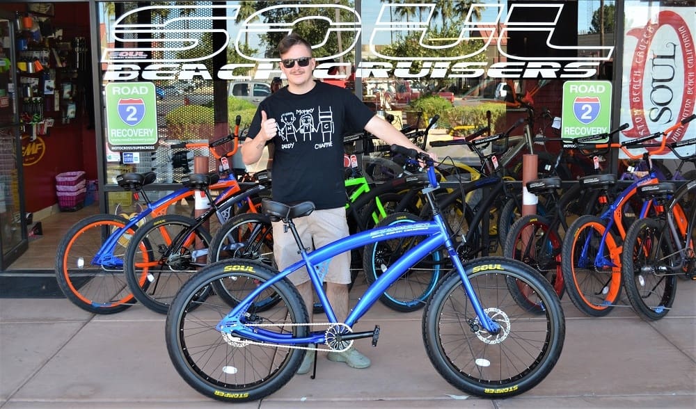 Man posing with blue bicycle outside store.