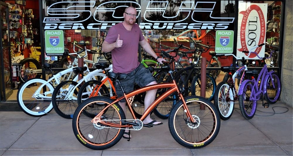 Man posing with bicycle outside bike shop.