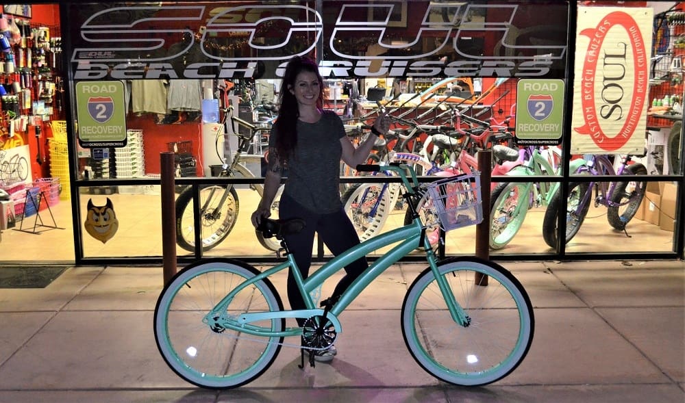 Woman standing with bicycle outside bike shop.