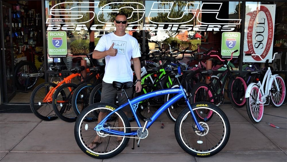 Man posing with blue bicycle outside store.