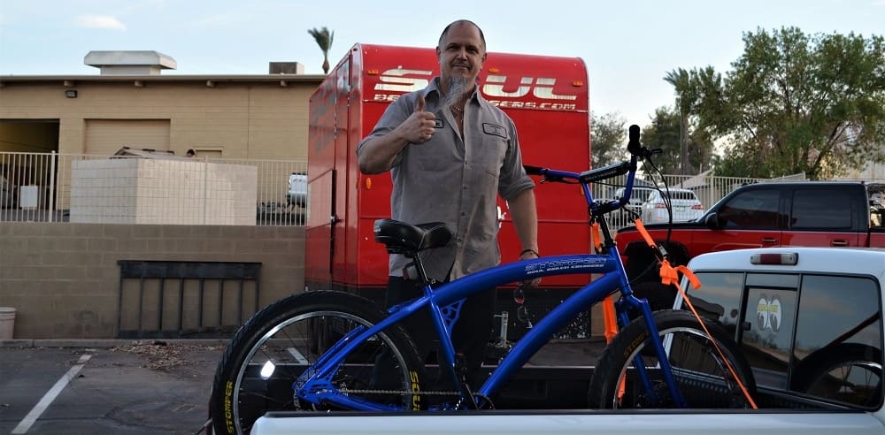 Man posing with blue bicycle outdoors.