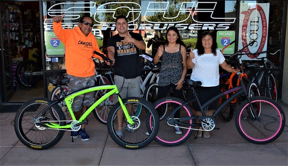 Group of people posing with bicycles outside shop.