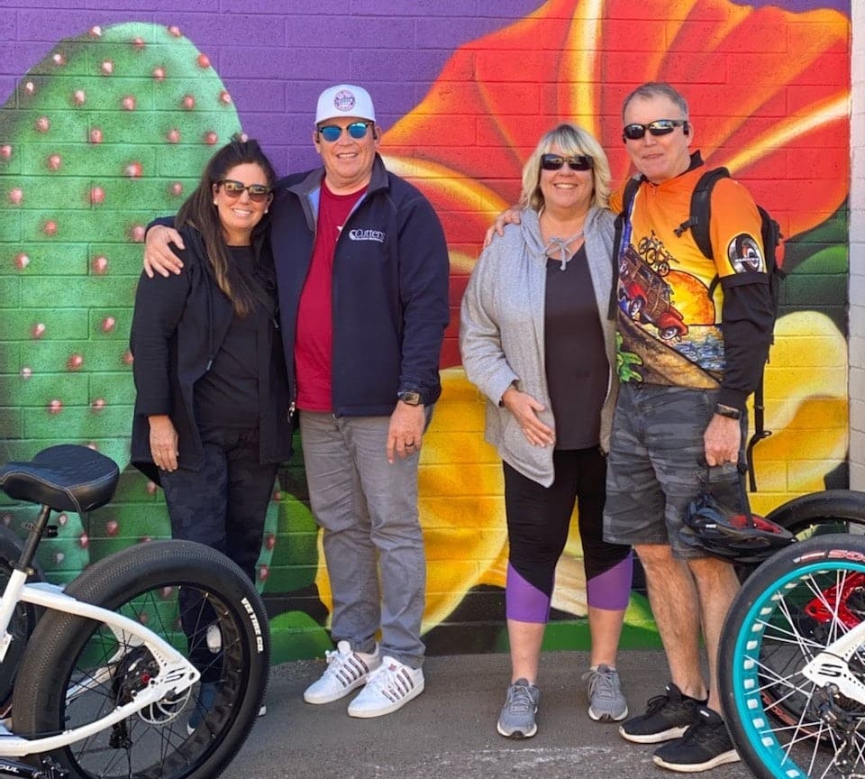 Four people posing in front of mural.