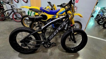 Black electric bike beside yellow motorcycles.