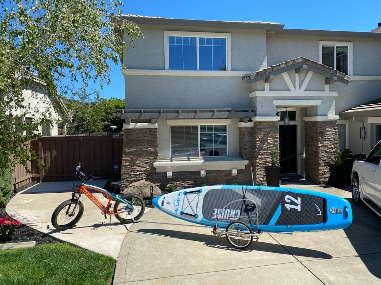 Bicycle towing paddleboard outside suburban house.